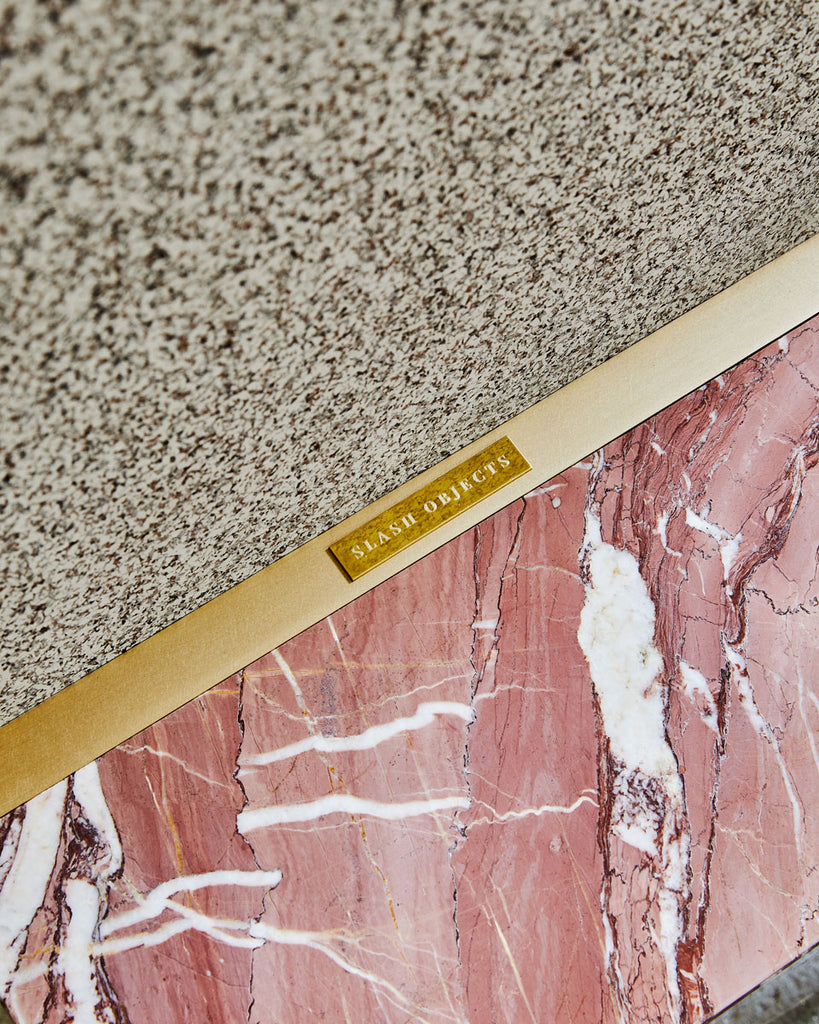 Standing mirror detail image with red jasper cube base, brass mirror frame, speckled beige rubber back and brass brand logo.