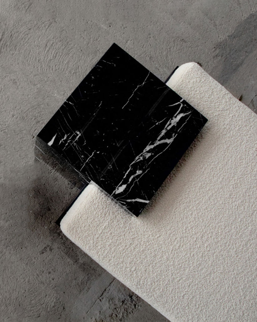  Detail image of bench showing cube nero marquina marble base, blackened steel structure and beige boucle fabric upholstered mattress.