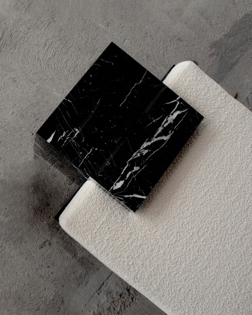 Detail image of bench showing cube nero marquina marble base, blackened steel structure and beige boucle fabric upholstered mattress.