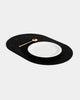Angled view of black rubber capsule placemat with white plate and brass spoon on white background.