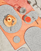 Spring table setting with speckled grey rubber capsule placemats, capsule trivets and round coasters on concrete and terracotta surface. The setting is styled with half cut grapefruit, peach, spoon, fork and a glass of water with metallic straw.
