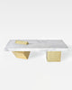 Coffee table with rectangular white carrara marble top and two cube brass legs. One of the brass cube leg is standing on its knife-edge slicing through marble top.