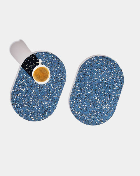 Two capsule speckled blue rubber trivets on white surface. One trivet has a white espresso cup on it.